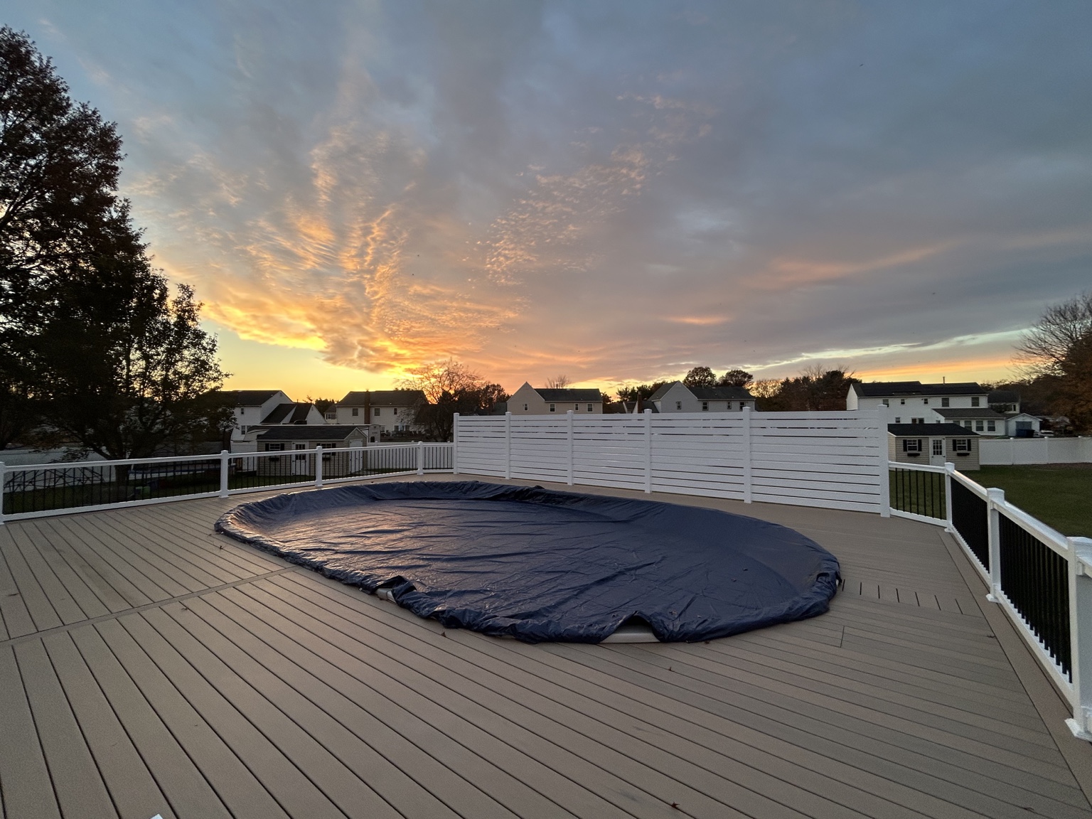 Composite pool deck at sunset with white railings, black balusters and a white privacy screen