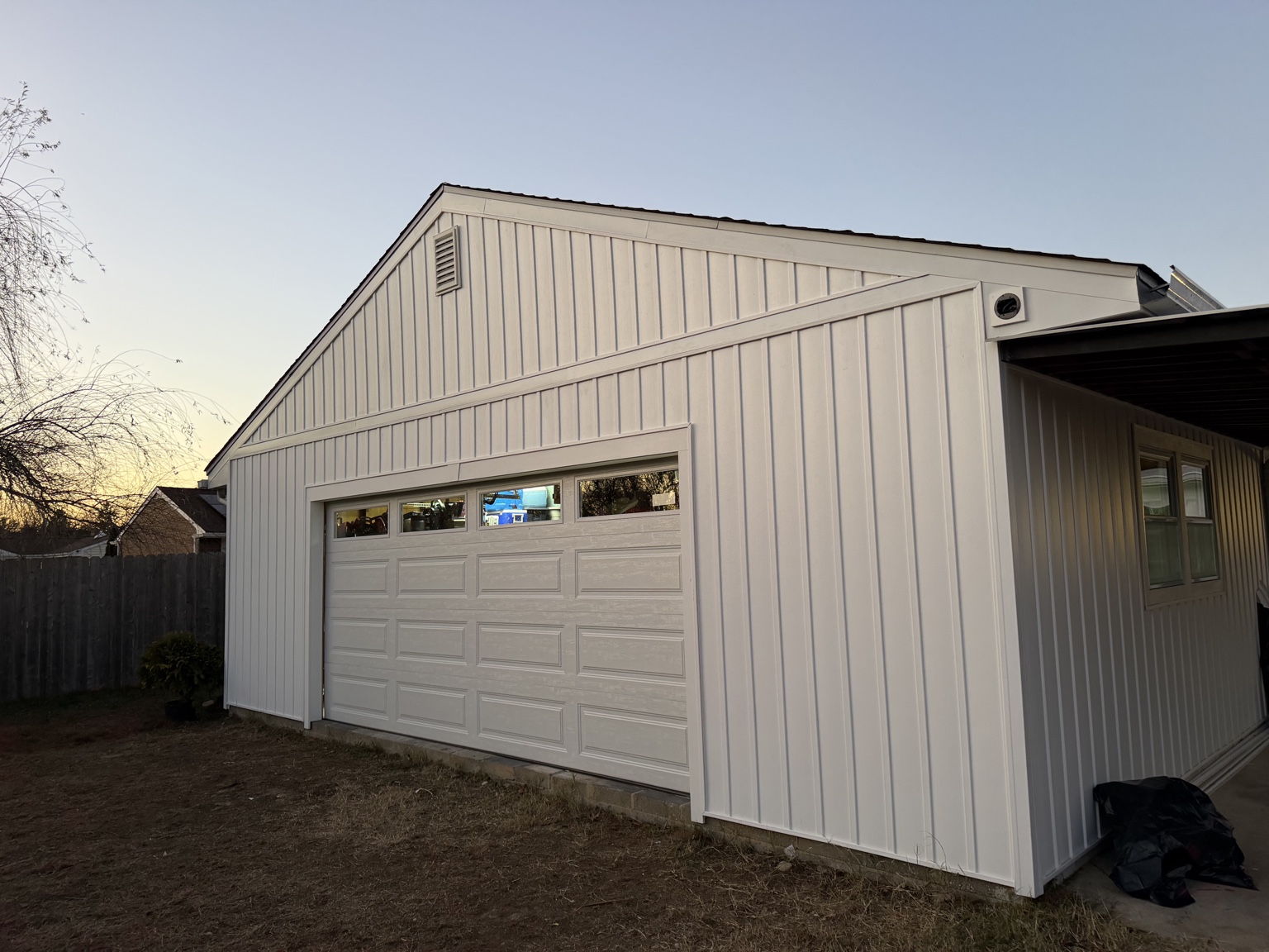 Garage exterior with white vertical siding, wide white trim and a matching garage door